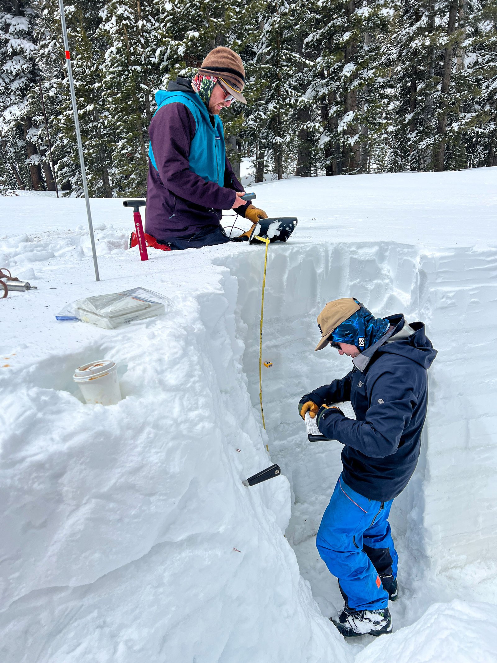 openai a researcher stands in a snowy trench taking notes, while a second researcher drops a yellow measure down from the surface level