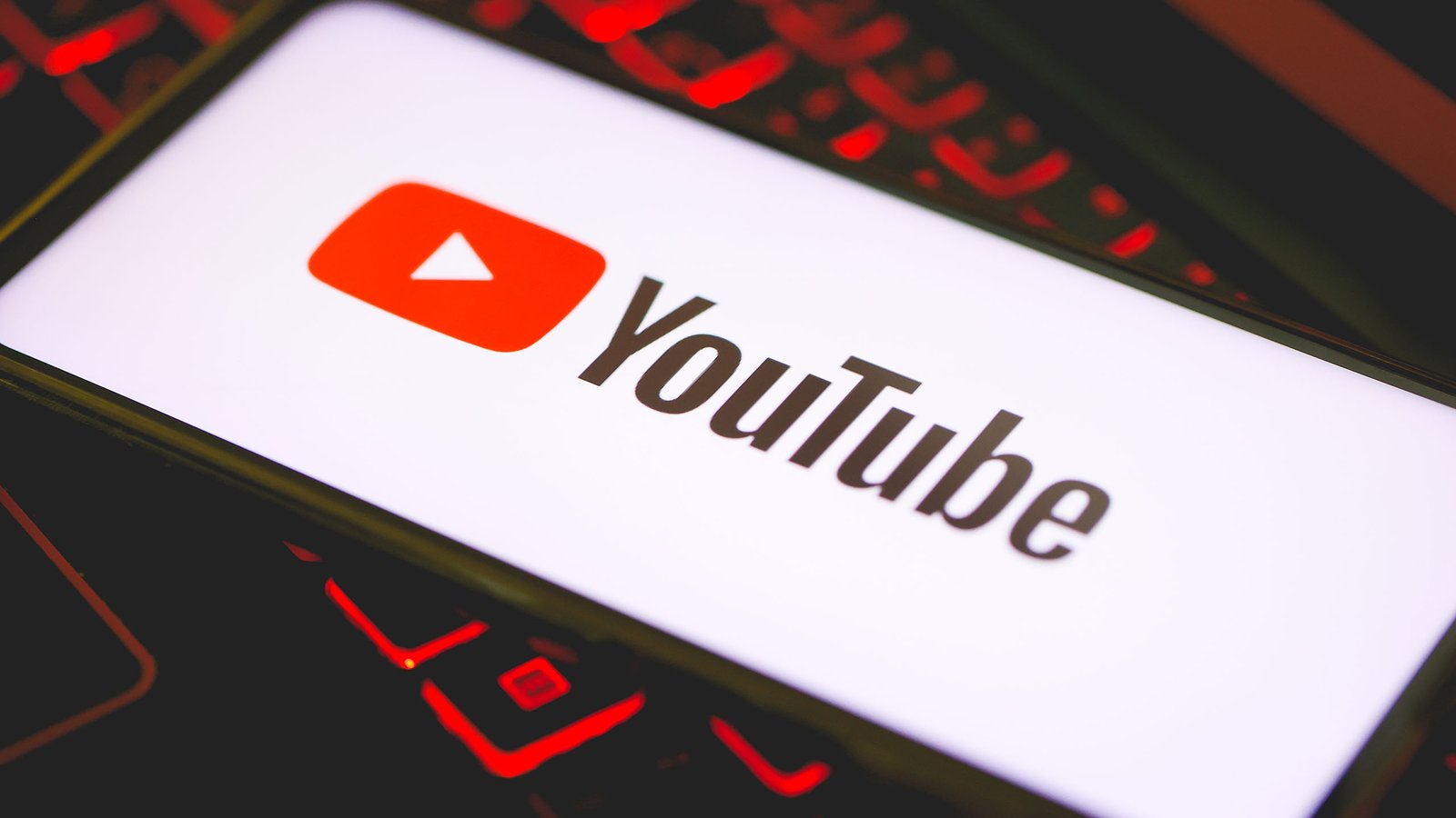 machine learning Das Logo von YouTube auf dem Bildschirm eines Smartphones, das über einer Tastatur eines Gaming-Laptops steht.
